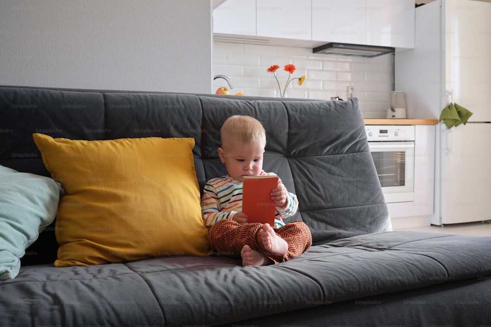 a baby sitting on a couch playing with a tablet