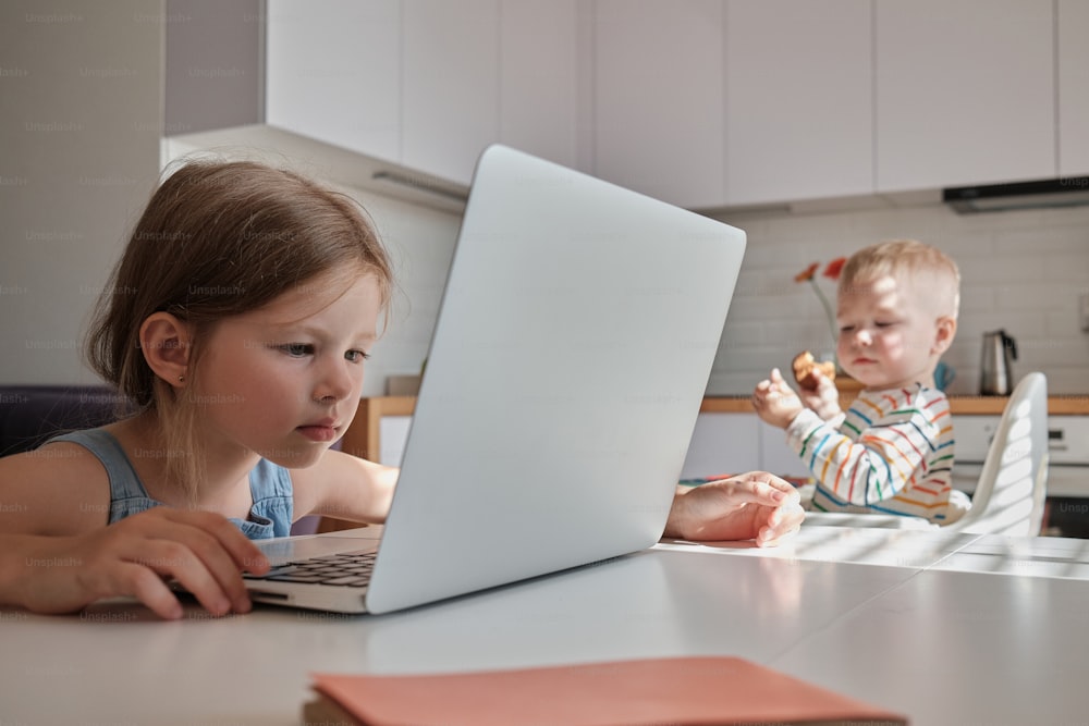노트북이 있는 테이블에 앉아 있는 두 어린 아이들