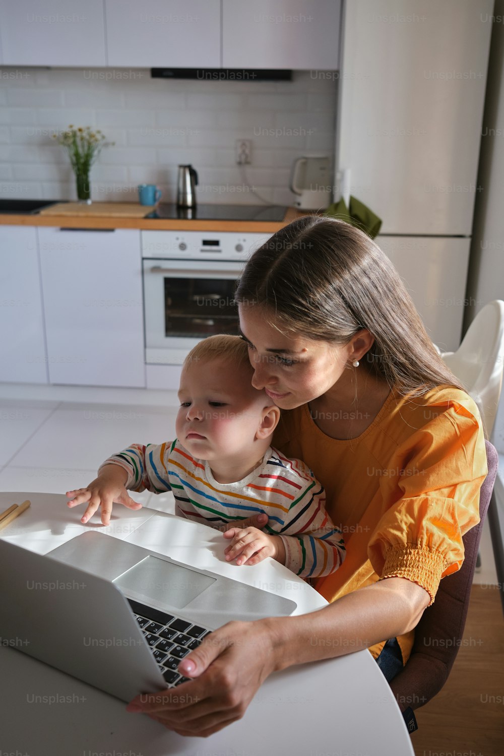 a woman sitting at a table with a baby in front of a laptop