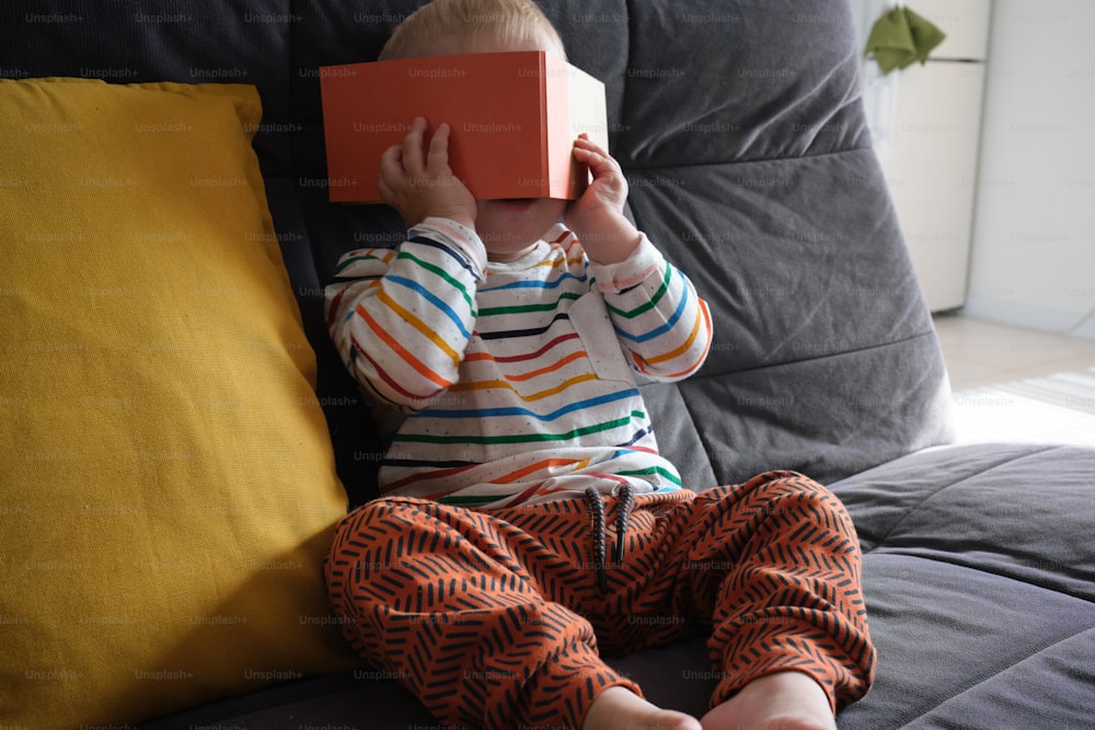 a little boy sitting on a couch holding a book