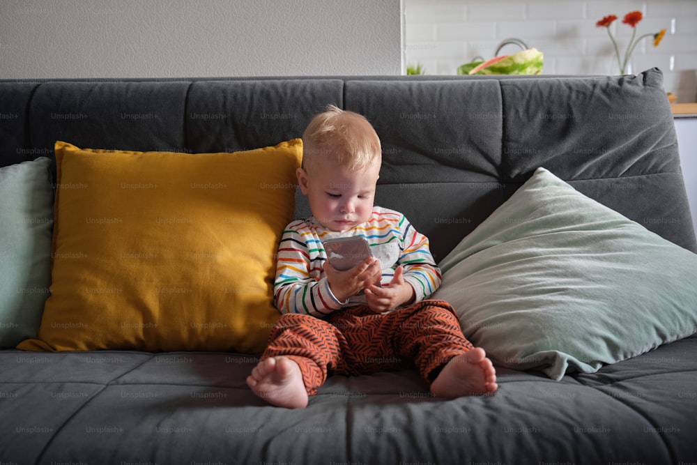 a baby sitting on a couch playing with a cell phone