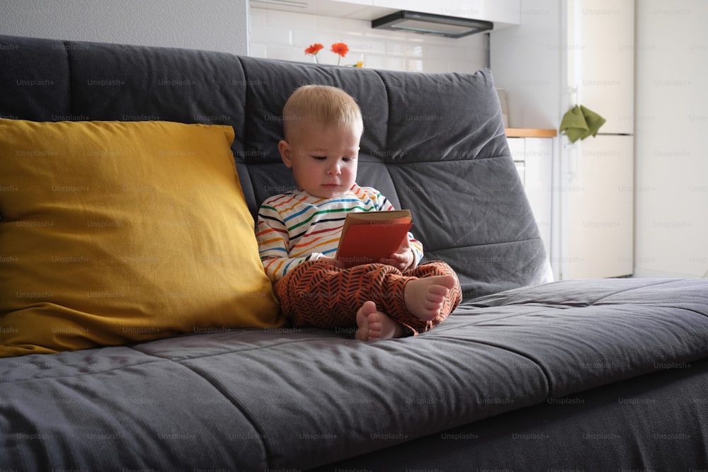 Ein kleiner Junge, der mit einem Tablet auf einer Couch sitzt