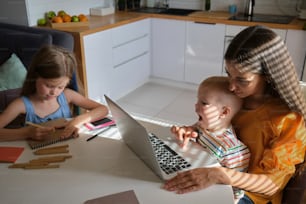 ノートパソコンを持ってテーブルに座る女性と2人の子供