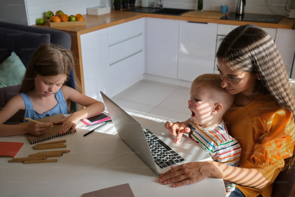 Una mujer y dos niños sentados en una mesa con una computadora portátil