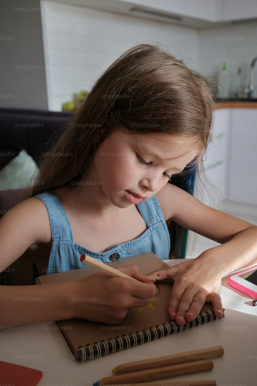 Ein kleines Mädchen sitzt an einem Tisch mit einem Notizbuch und Bleistiften