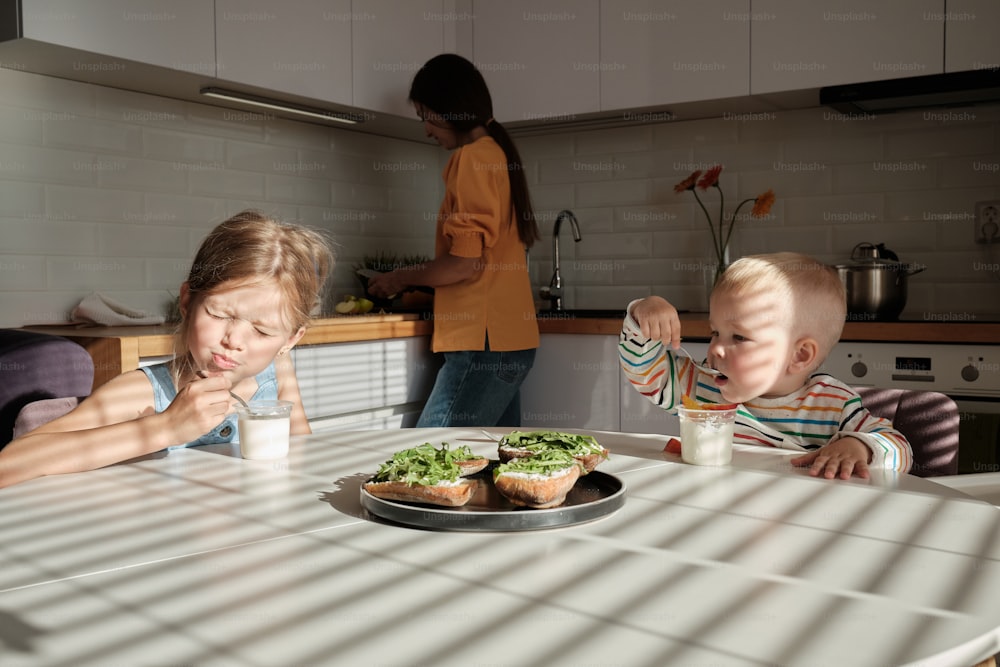 a couple of kids sitting at a table with a plate of food