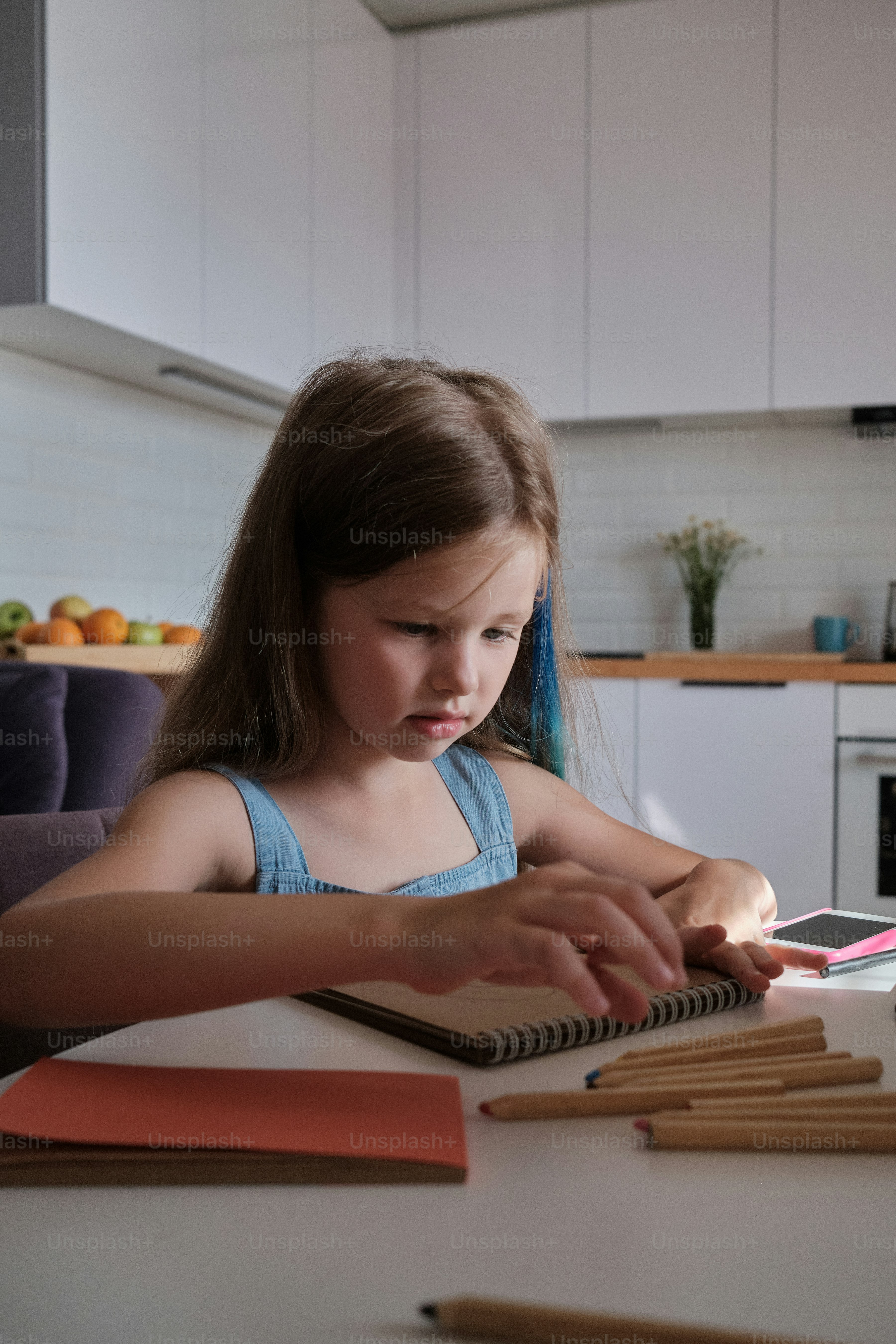 a little girl sitting at a table with some pencils