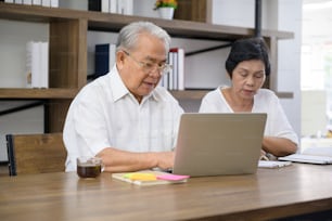Una feliz pareja asiática de la tercera edad pasa tiempo navegando por Internet y hablando con la familia por la cámara web, concepto de jubilación.