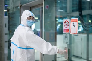 Un uomo asiatico indossa una tuta DPI nell'ascensore dell'aeroporto, viaggi di sicurezza, protezione covid-19, concetto di distanziamento sociale.
