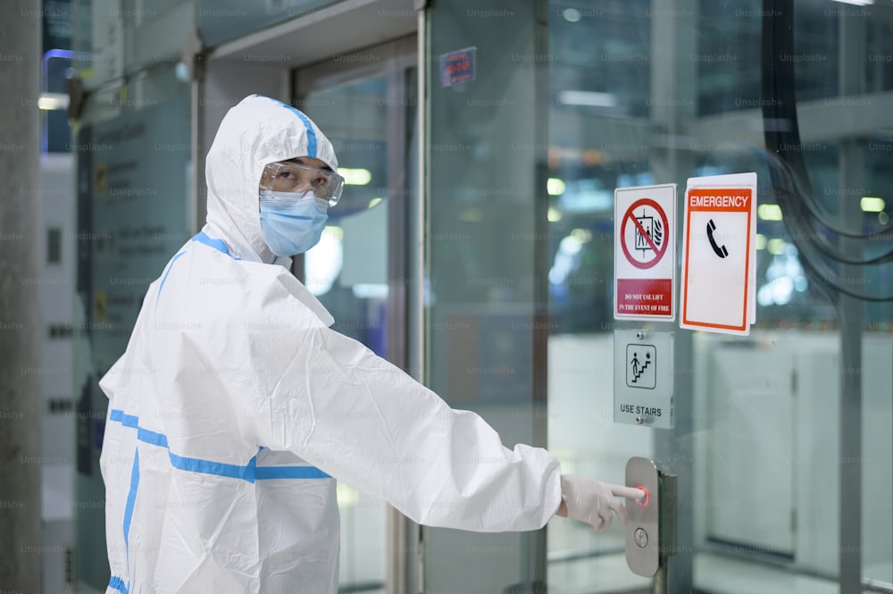 Un uomo asiatico indossa una tuta DPI nell'ascensore dell'aeroporto, viaggi di sicurezza, protezione covid-19, concetto di distanziamento sociale.