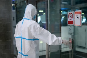 アジア人男性は空港のエレベーターでPPEスーツを着ています , 安全旅行 , covid-19保護 , 社会的距離のコンセプト .