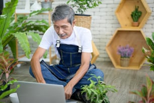 Hombre jubilado asiático mayor feliz con computadora portátil se relaja y disfruta de la actividad de ocio en el jardín de su casa.