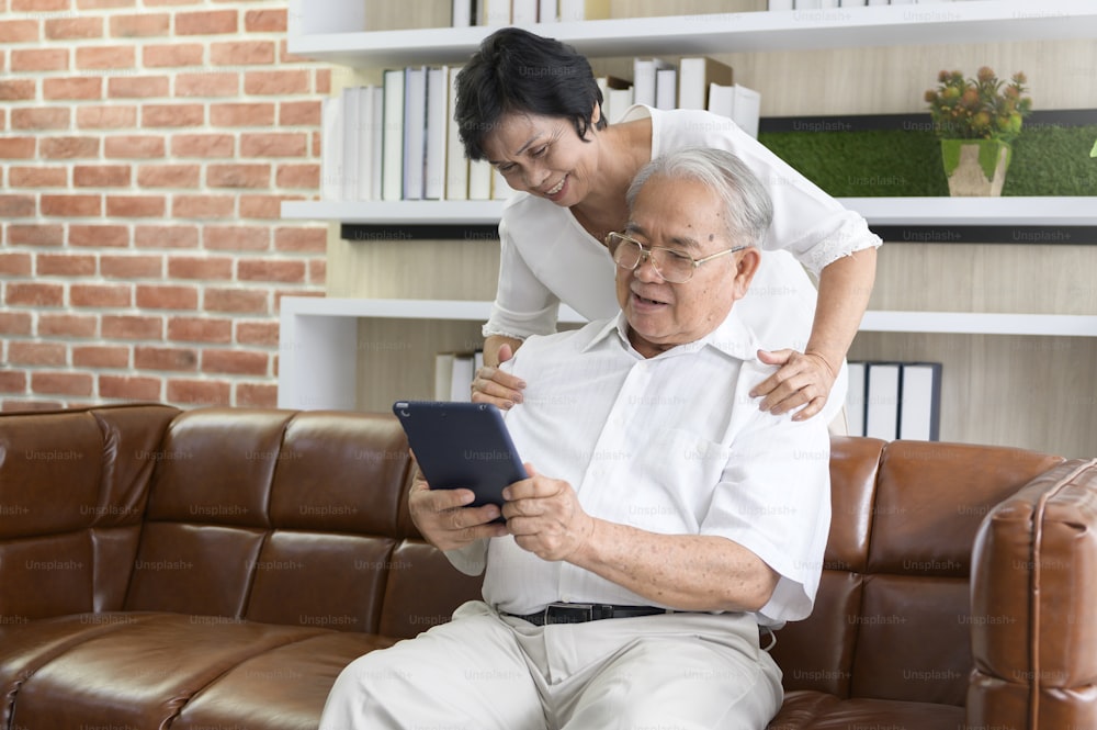 A happy senior Asian couple is using tablet and talking with family on webcam at home, retirement concept.