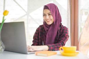 Donna musulmana con hijab sta lavorando con un computer portatile in una caffetteria