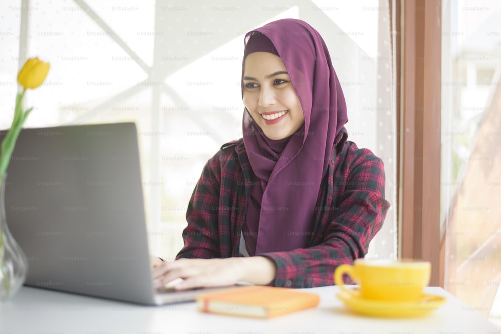 Una mujer musulmana con hiyab está trabajando con una computadora portátil en una cafetería