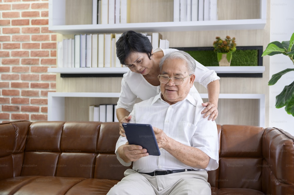 A happy senior Asian couple is using tablet and talking with family on webcam at home, retirement concept.