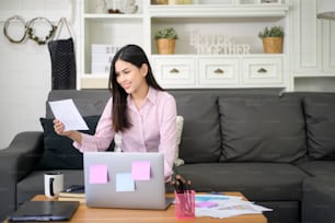 A business woman is working with laptop computer and analyzing business growth graph data in living room, Work from home , business technology concept .