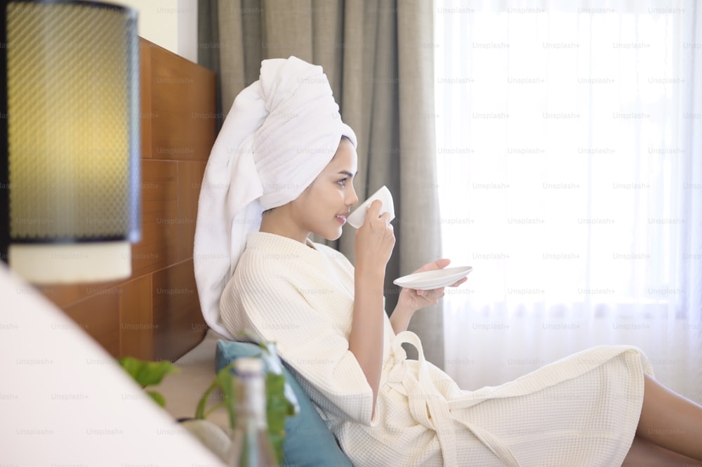 Eine entspannte Frau mit weißem Bademantel und Handtuch beim Kaffee am Morgen