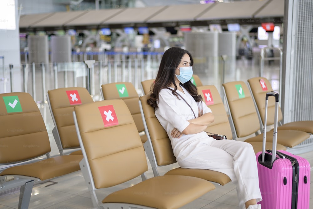 여행자 여성이 국제공항에서 보호 마스크를 착용하고 있으며, Covid-19 전염병, 안전 여행, 사회적 거리두기 프로토콜, 뉴노멀 여행 개념에 따라 여행하고 있습니다.