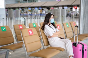 여행자 여성이 국제공항에서 보호 마스크를 착용하고 있으며, Covid-19 전염병, 안전 여행, 사회적 거리두기 프로토콜, 뉴노멀 여행 개념에 따라 여행하고 있습니다.