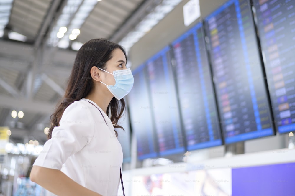旅行者の女性は国際空港で保護マスクを着用しています、Covid-19パンデミック下での旅行、安全旅行、社会的距離のプロトコル、ニューノーマル旅行のコンセプト。