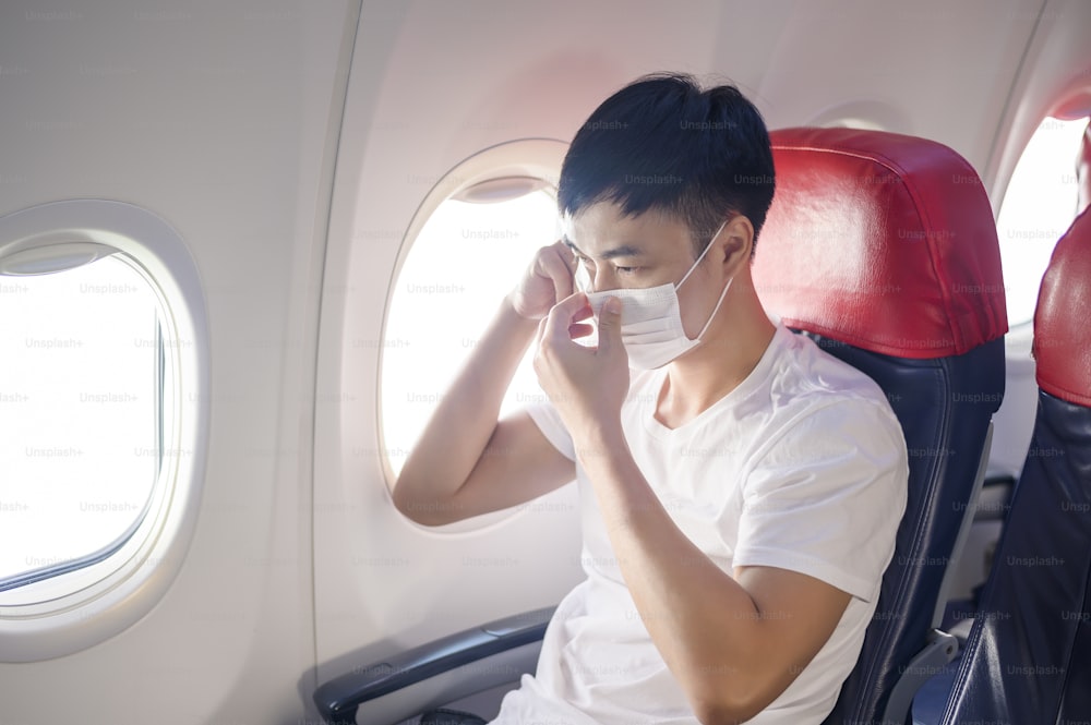 여행하는 남자가 항공기에서 보호 마스크를 착용하고, Covid-19 전염병에 따른 여행, 안전 여행, 사회적 거리두기 프로토콜, 뉴 노멀 여행 컨셉
