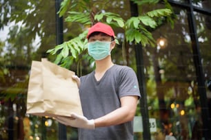Un fattorino asiatico indossa una maschera per il viso, tenendo la borsa della spesa, concetto di consegna a domicilio di sicurezza