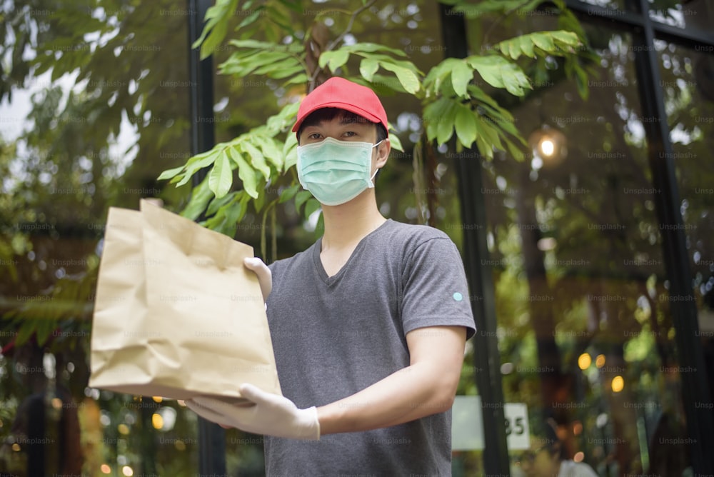 Ein asiatischer Zusteller trägt Gesichtsmaske, hält Einkaufstüte, Sicherheits-Hauslieferkonzept