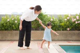 Una madre asiática está sosteniendo la mano de su bebé para caminar a un lado de la piscina, la familia, la paternidad, el concepto de seguridad en el hogar.