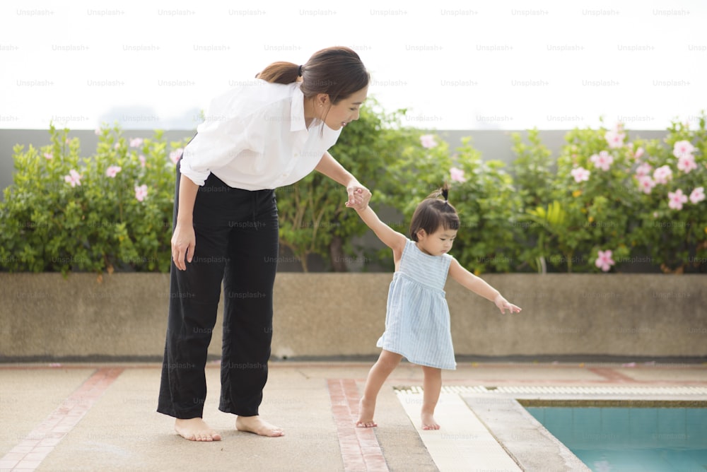 Eine asiatische Mutter hält ihr kleines Mädchen an der Hand, um neben dem Pool, der Familie, der Elternschaft und dem Sicherheitskonzept zu Hause zu gehen.
