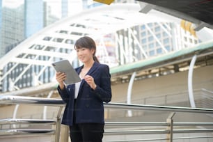 hermosa joven mujer de negocios asiática está usando la tableta en la ciudad moderna