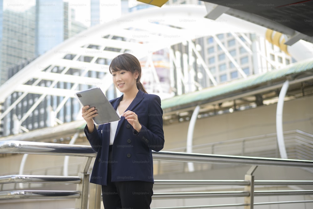 美しい若いアジア ビジネス女性は、近代的な都市でタブレットを使用しています。