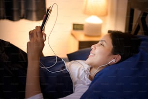 A young woman is using tablet , watching movies or video call to her friends or family in her bedroom , night Light