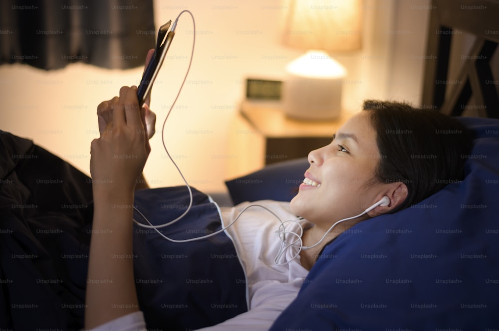 Eine junge Frau benutzt Tablet, schaut Filme oder Videoanrufe mit ihren Freunden oder Familie in ihrem Schlafzimmer, Nachtlicht