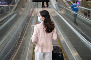 A business woman is wearing protective mask in International airport, travel under Covid-19 pandemic, safety travels, social distancing protocol, New normal travel concept.