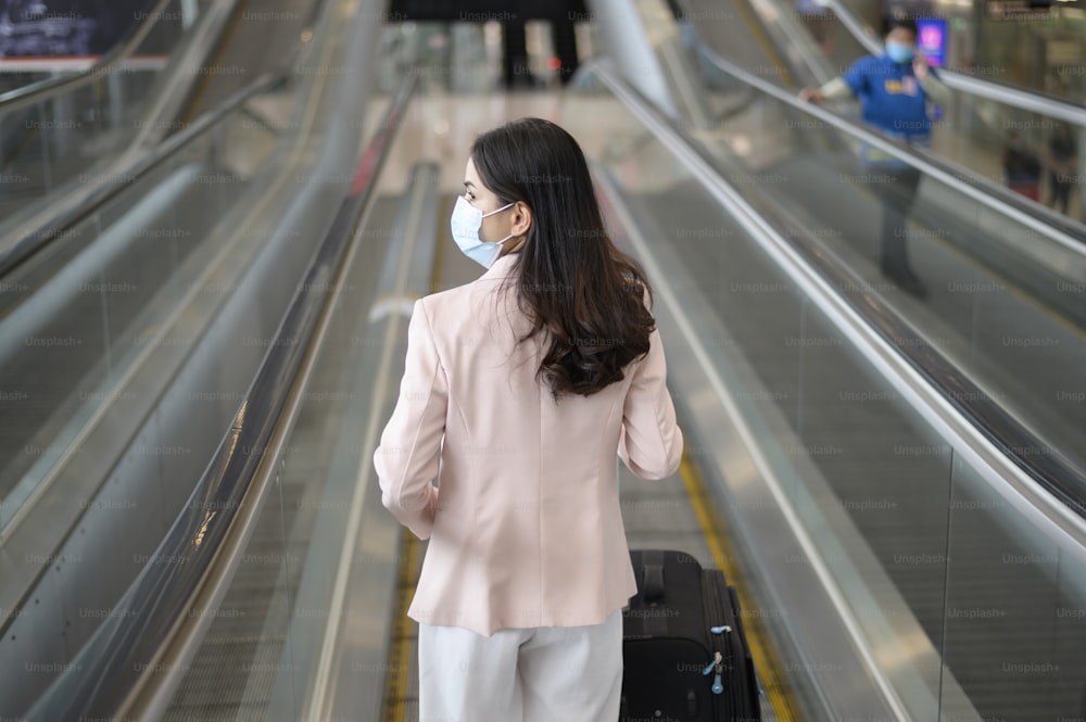 Una donna d'affari indossa una maschera protettiva nell'aeroporto internazionale, viaggia sotto la pandemia di Covid-19, viaggi di sicurezza, protocollo di distanziamento sociale, nuovo concetto di viaggio normale.