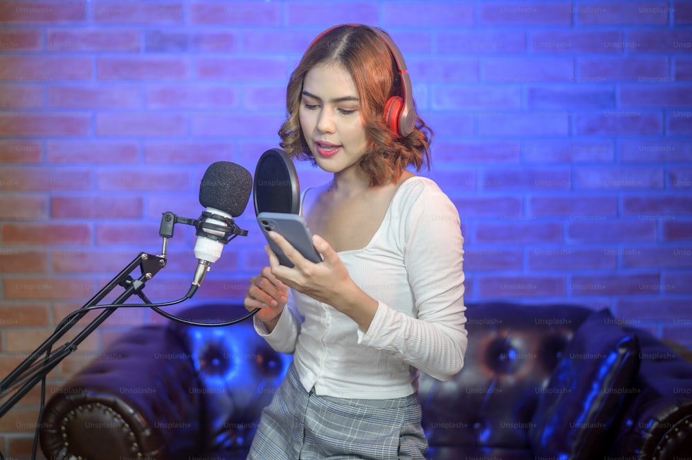 Una joven cantante sonriente que usa auriculares con un micrófono mientras graba una canción en un estudio de música con luces de colores.