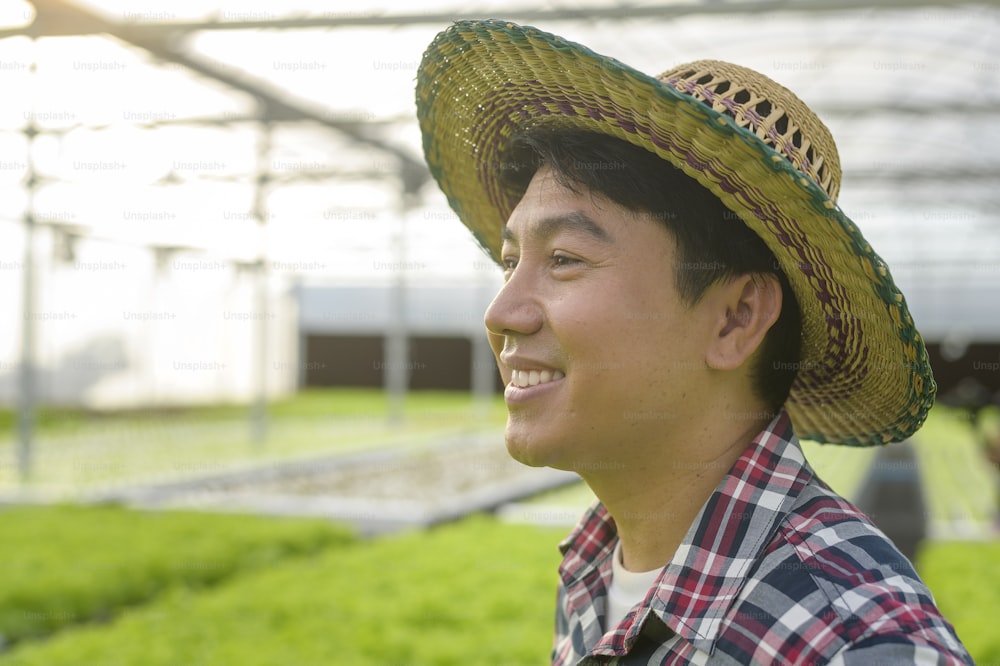Agricultor masculino feliz que trabalha na fazenda de estufa hidropônica, alimentos limpos e conceito de alimentação saudável