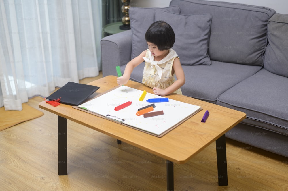 Menina que desenha com lápis de cor na sala de estar em casa.