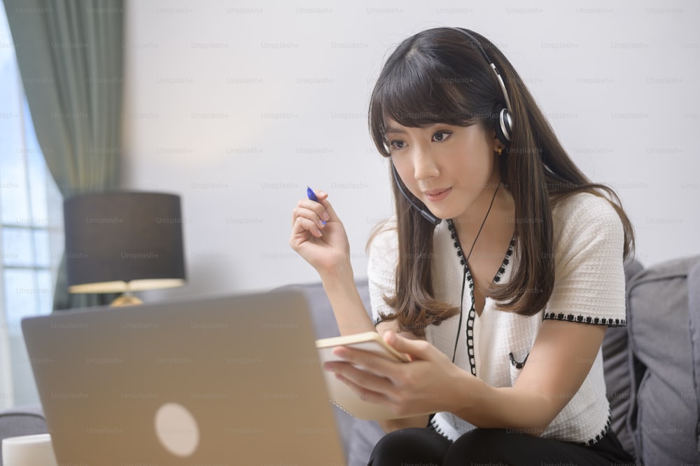Eine schöne junge Frau mit Headset telefoniert zu Hause per Computer