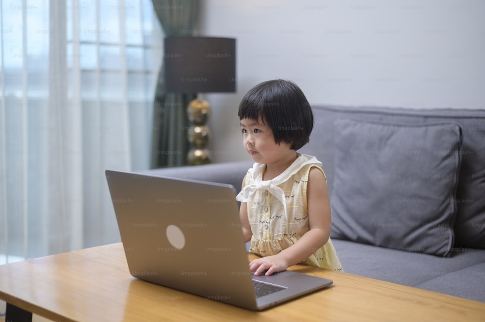 Ein asiatisches glückliches Mädchen mit Laptop für das Lernen online über das Internet zu Hause. E-Learning Konzept
