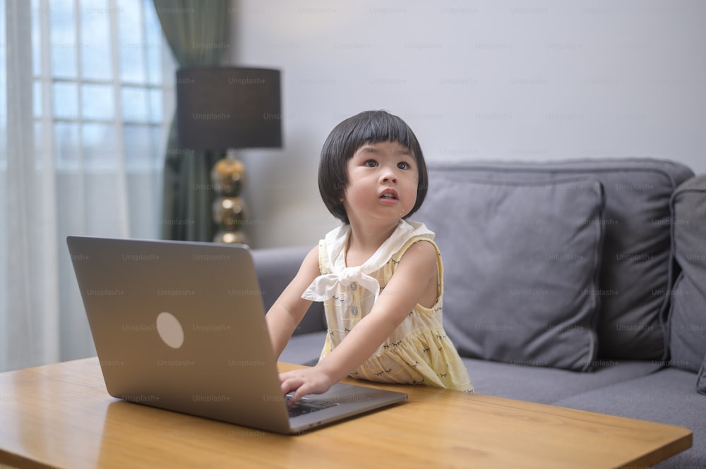 Uma menina asiática feliz usando laptop para estudar on-line via internet em casa. Conceito de E-learning