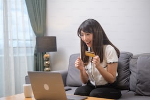 Uma jovem mulher bonita está usando cartão de crédito para compras on-line no site da internet em casa, conceito de comércio eletrônico