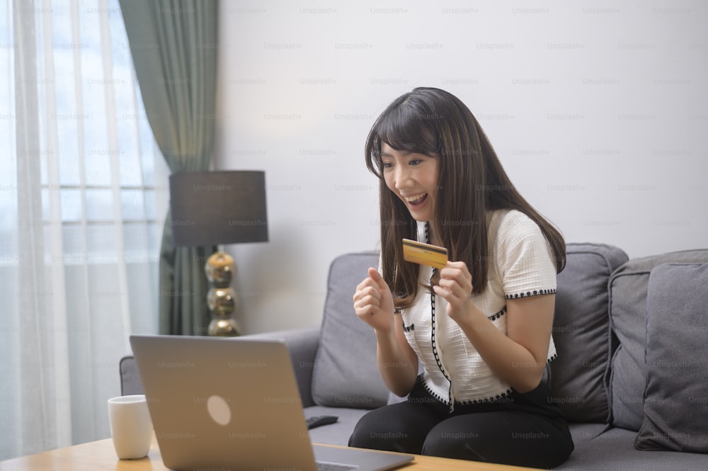 Une belle jeune femme utilise une carte de crédit pour les achats en ligne sur le site Internet à la maison, concept de commerce électronique
