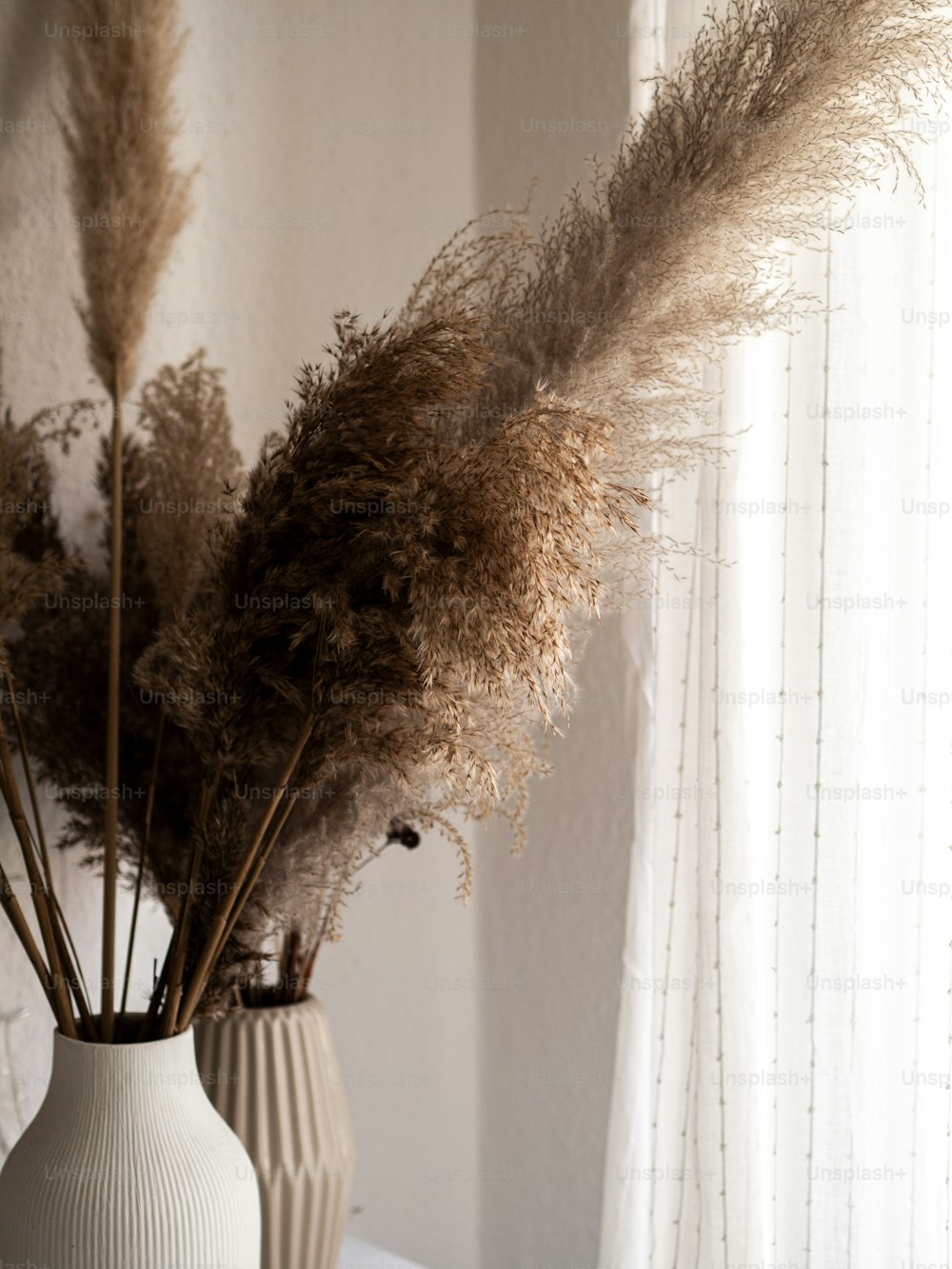 two vases with dried plants in them on a table