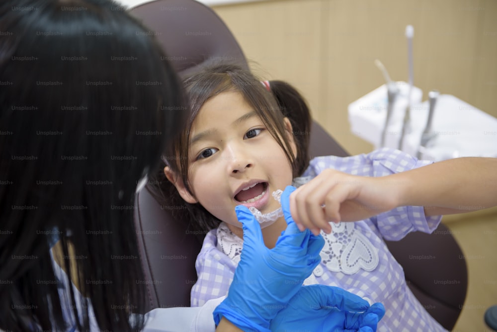 歯科医院で小さな女の子にインビザラインを見せている女性歯科医、歯の検診、健康な歯のコンセプト
