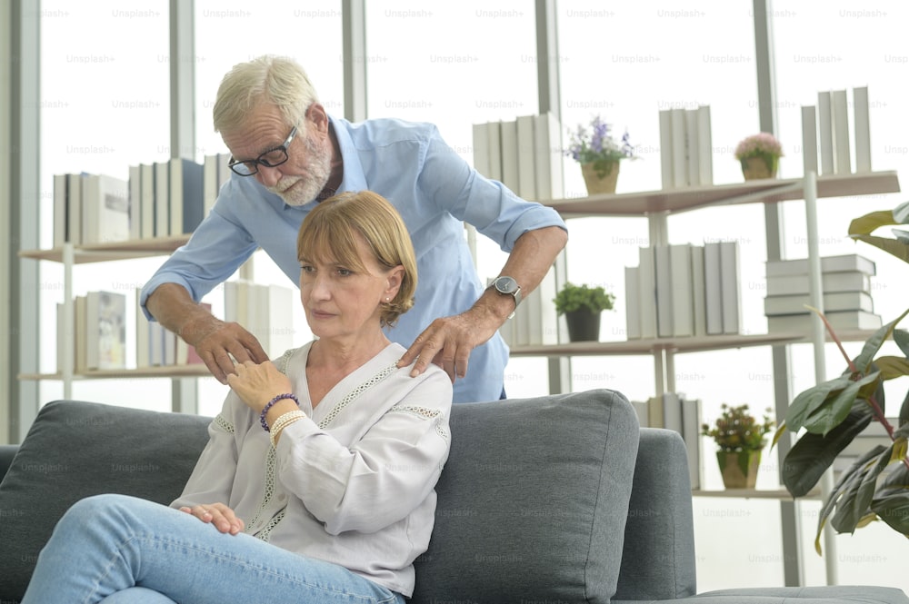 Uomo caucasico anziano che fa il massaggio per sua moglie in soggiorno