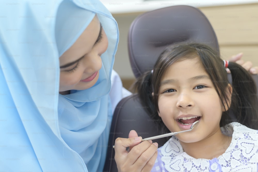 歯科医院でイスラム教徒の歯科医に歯を診てもらったかわいい女の子、歯の検診、健康な歯のコンセプト