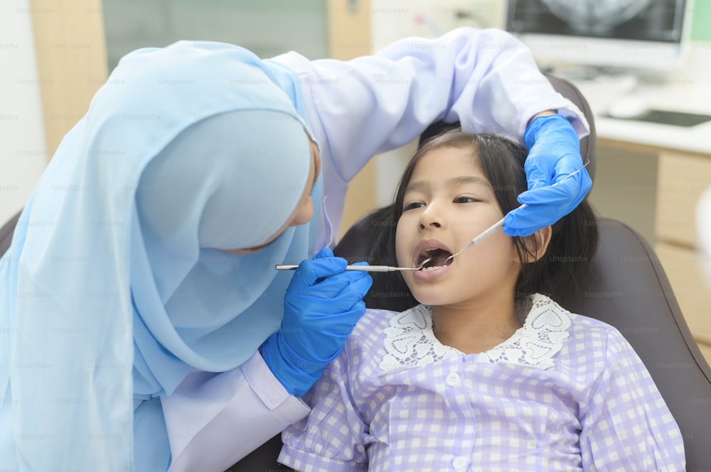 Una niña linda que tiene dientes examinados por un dentista musulmán en una clínica dental, chequeo de dientes y concepto de dientes sanos