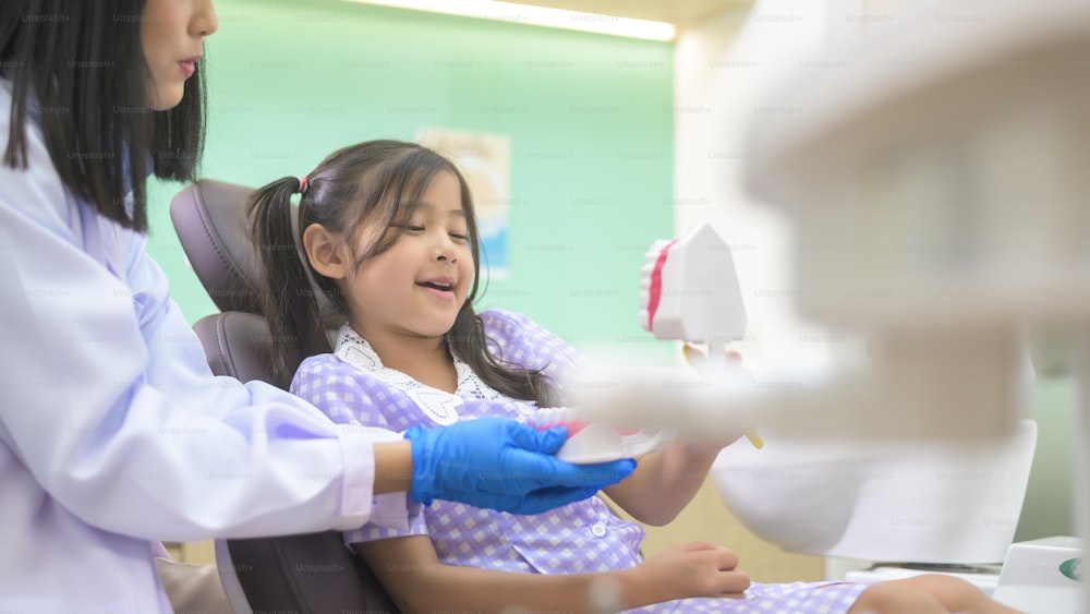 치과 진료소에서 어린 소녀에게 양치질하는 방법을 시연하는 여성 치과 의사, 치아 검진 및 건강한 치아 개념